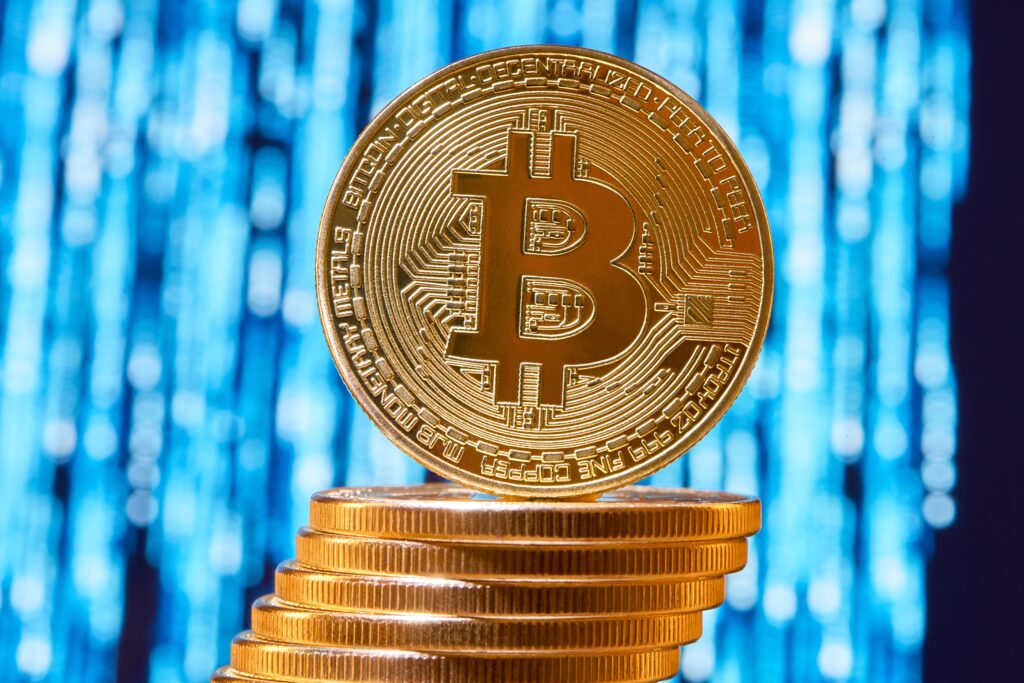 One bitcoin on edge placed on stack of golden bitcoins with blurred blue circuit on background